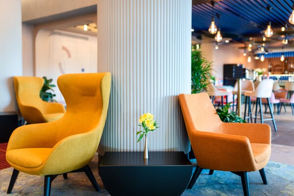 Un vestíbulo moderno con dos sillones amarillos, una mesita negra y un jarrón con flores amarillas.