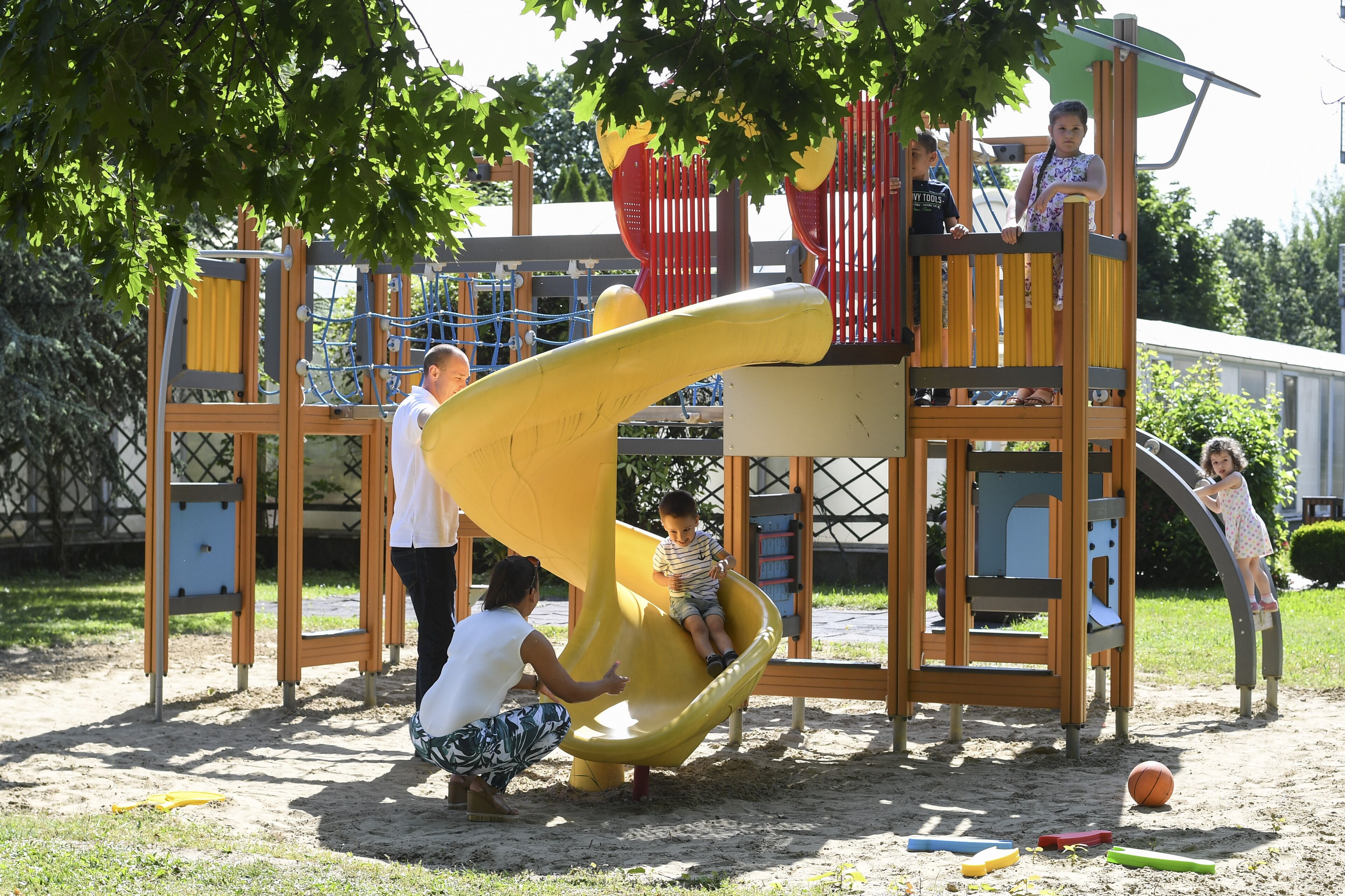 Une aire de jeux avec un toboggan jaune, des structures d’escalade et un espace de jeux abrité.