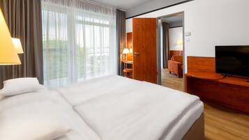 A hotel room with a large bed, a desk with a television, a chair, and a bathroom visible through an open door.