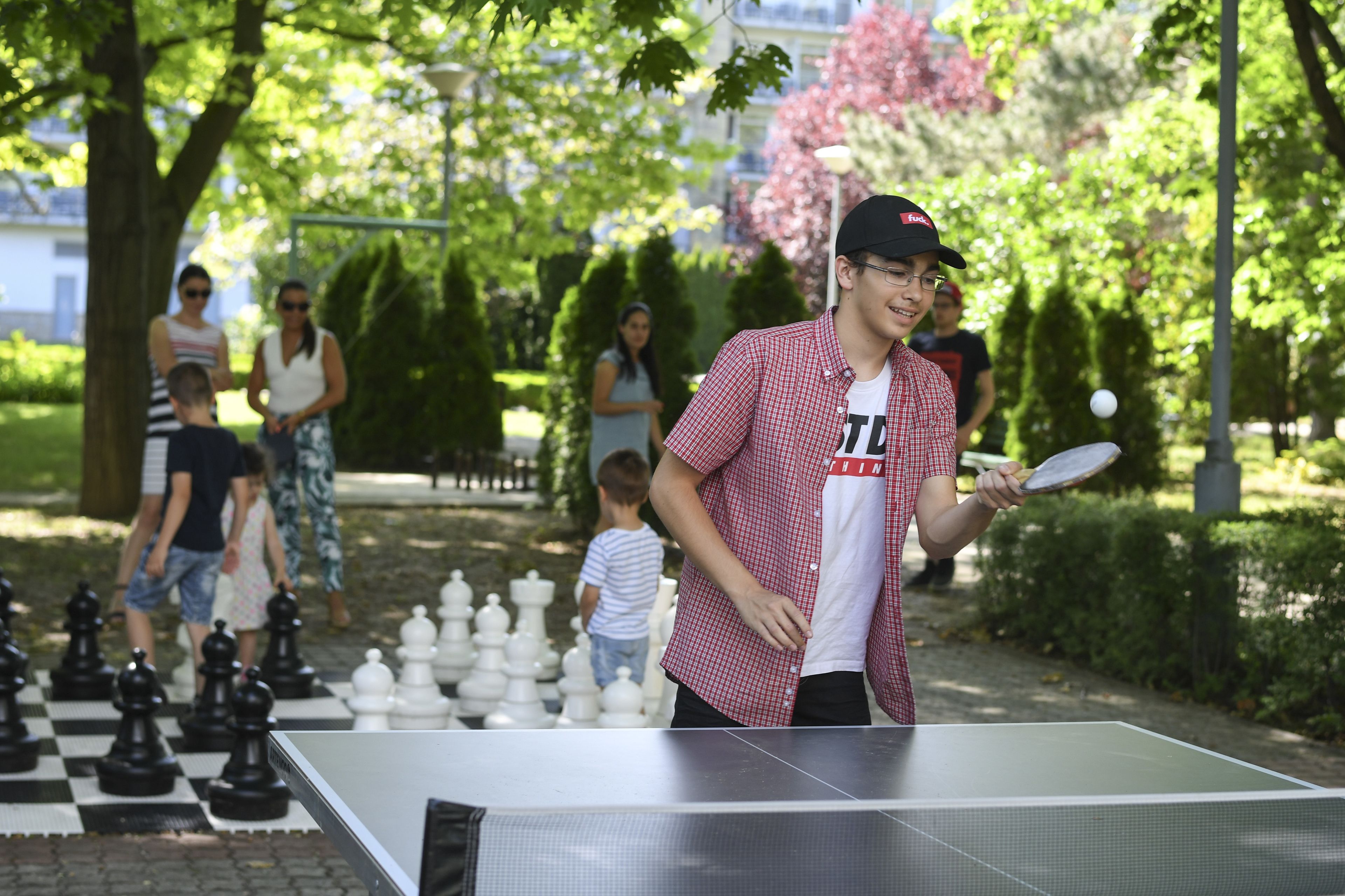 Una persona jugando ping pong al aire libre, con una mesa a cuadros y una pelota.