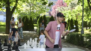 Una persona jugando ping pong al aire libre, con una mesa a cuadros y una pelota.