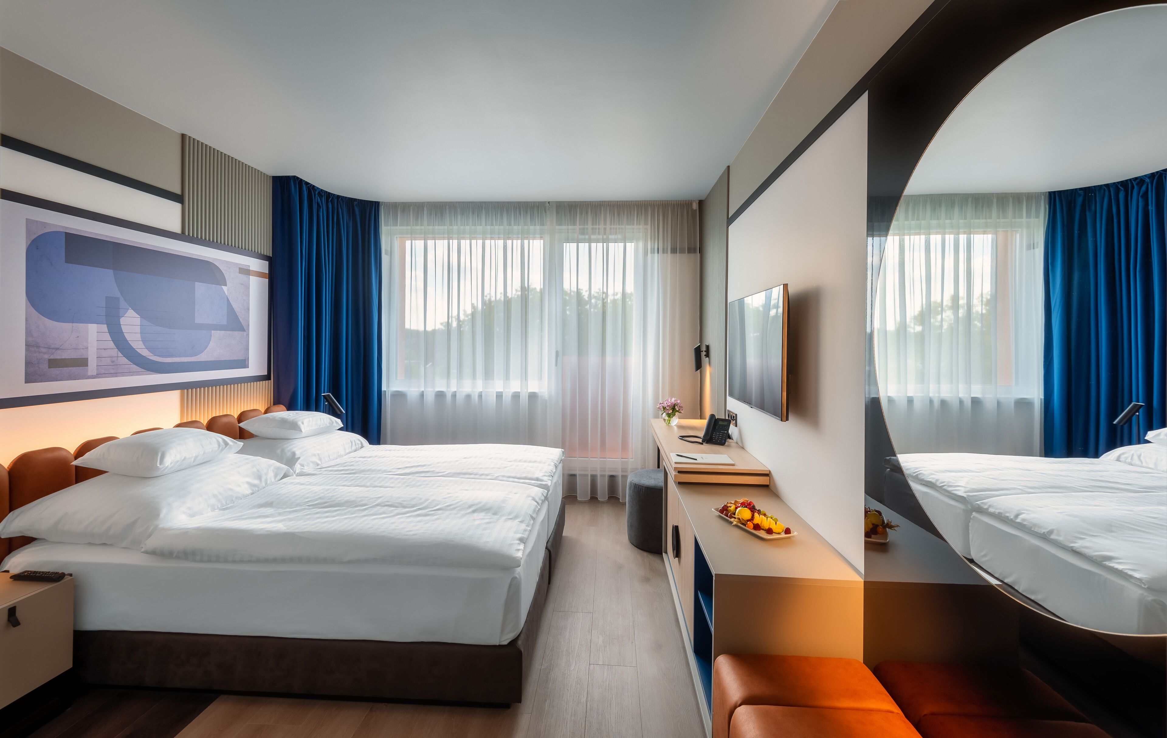 Habitación de hotel moderna con una cama grande, un escritorio con espejo y un ventanal con cortinas.