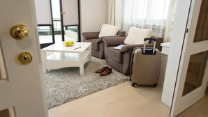 A hotel room with a sofa, a small table, a suitcase, and a view of the outside.