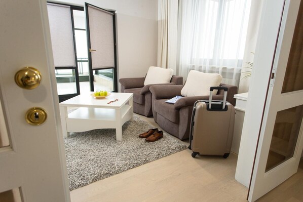 A hotel room with a sofa, a small table, a suitcase, and a view of the outside. - Hotel Hunguest Fenyo (Miercurea - Ciuc)