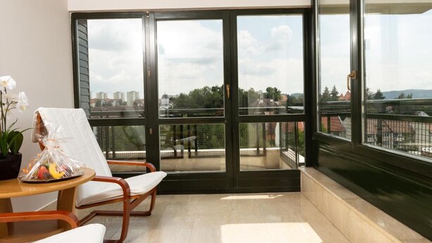 A balcony with a view of a cityscape, a wooden chair, a small table with a plant, and a potted orchid. - Hotel Hunguest Fenyo (Miercurea - Ciuc)