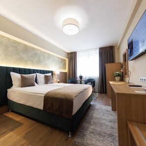 Una habitación de hotel moderna con una cama grande, un escritorio, una silla, un televisor y una ventana con cortinas.