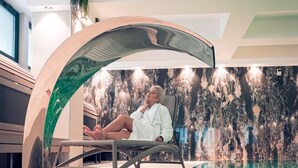 A person relaxing in a modern indoor pool area with a unique arch structure, a textured wall, and a clear pool.
