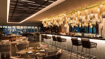 A modern bar area with high stools, a long counter, and hanging decorative lights.