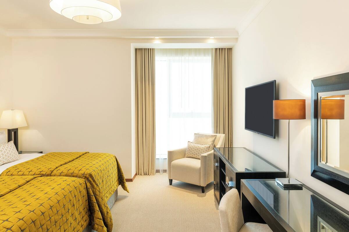 A hotel room with two beds, a sofa, a TV, and a desk.