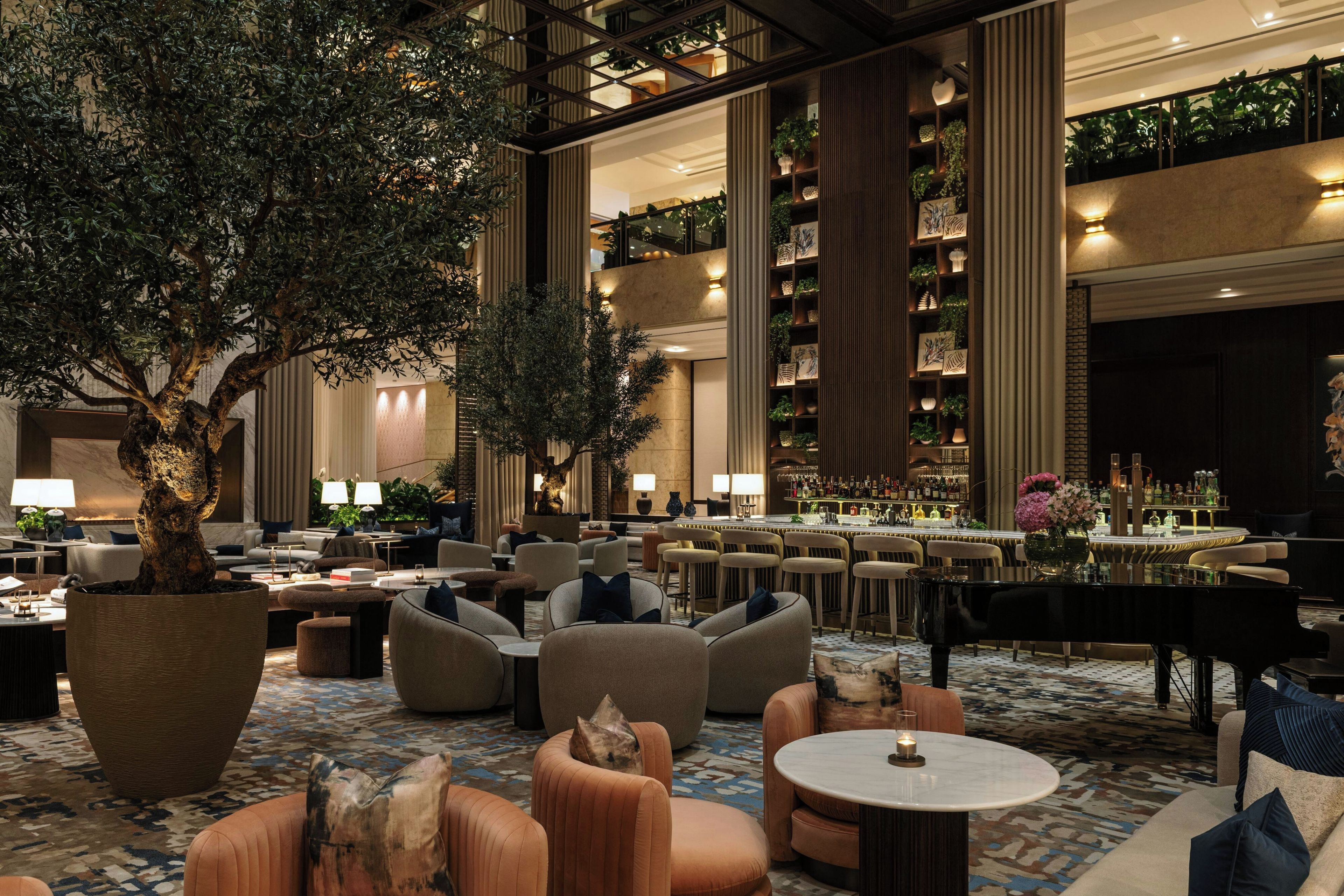 A spacious lobby with seating areas, a bar, and a large tree.