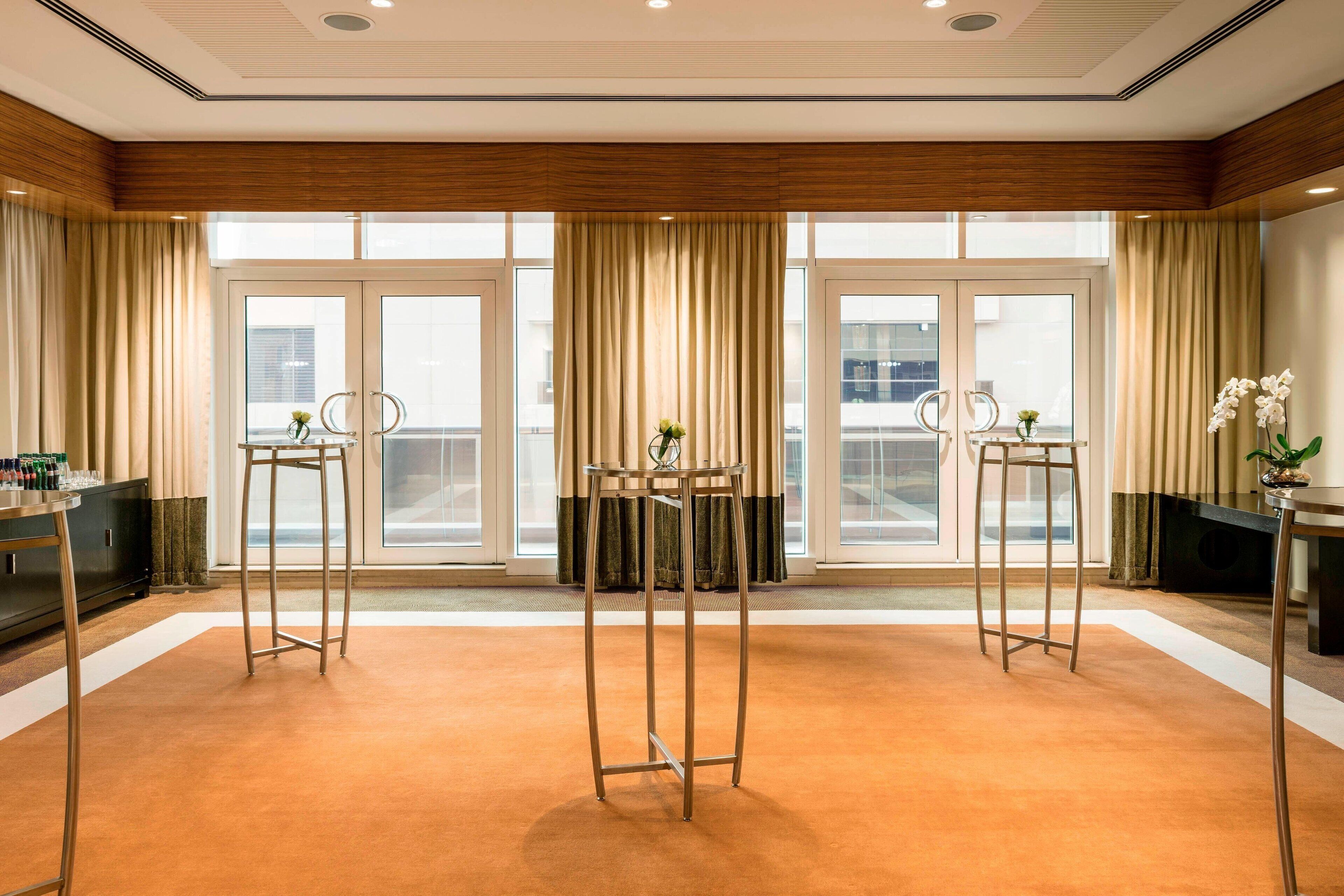 A spacious room with large windows, a central table with chairs, and two tall, metal stands.