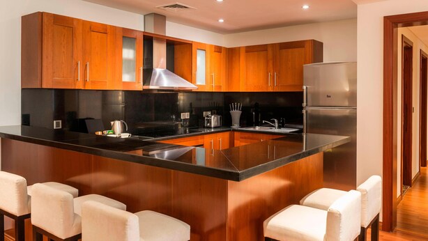 A modern kitchen with wooden cabinets, a central island with bar stools, stainless steel appliances, and recessed ceiling lighting. - Grosvenor House, a Luxury Collection Hotel, Dubai (Dubai)