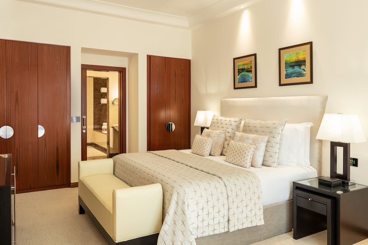 A hotel room with a large bed, bedside tables, a sofa, and wooden wardrobes.