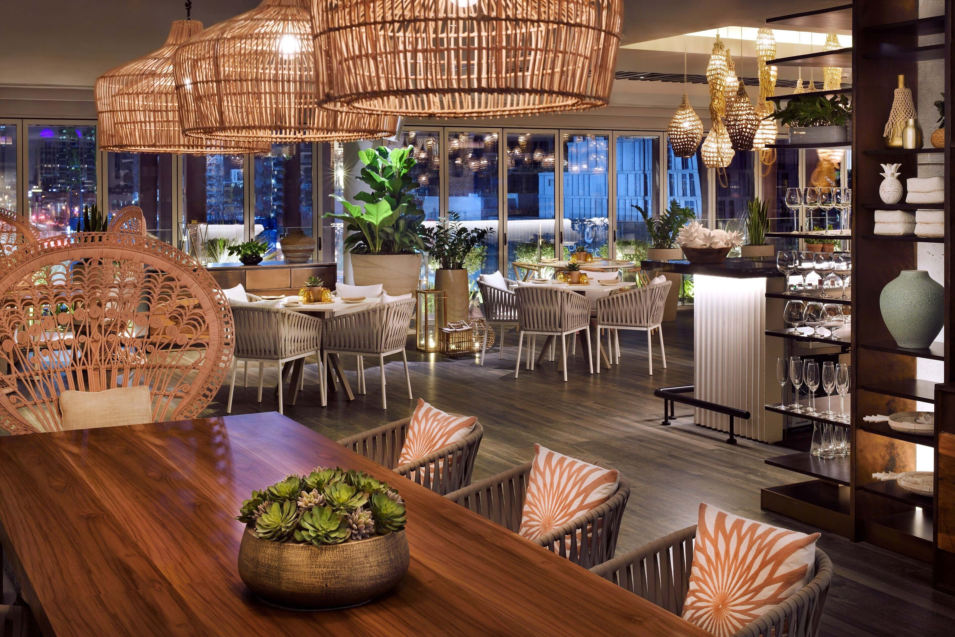 A modern dining area with wicker furniture, a wooden table, and hanging wicker chandeliers.