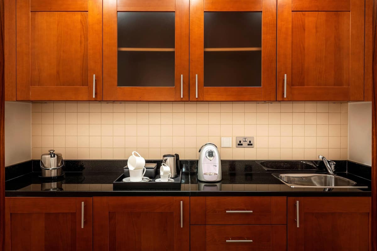 A kitchen with wooden cabinets, a black countertop, a kettle, a coffee maker, and a sink.