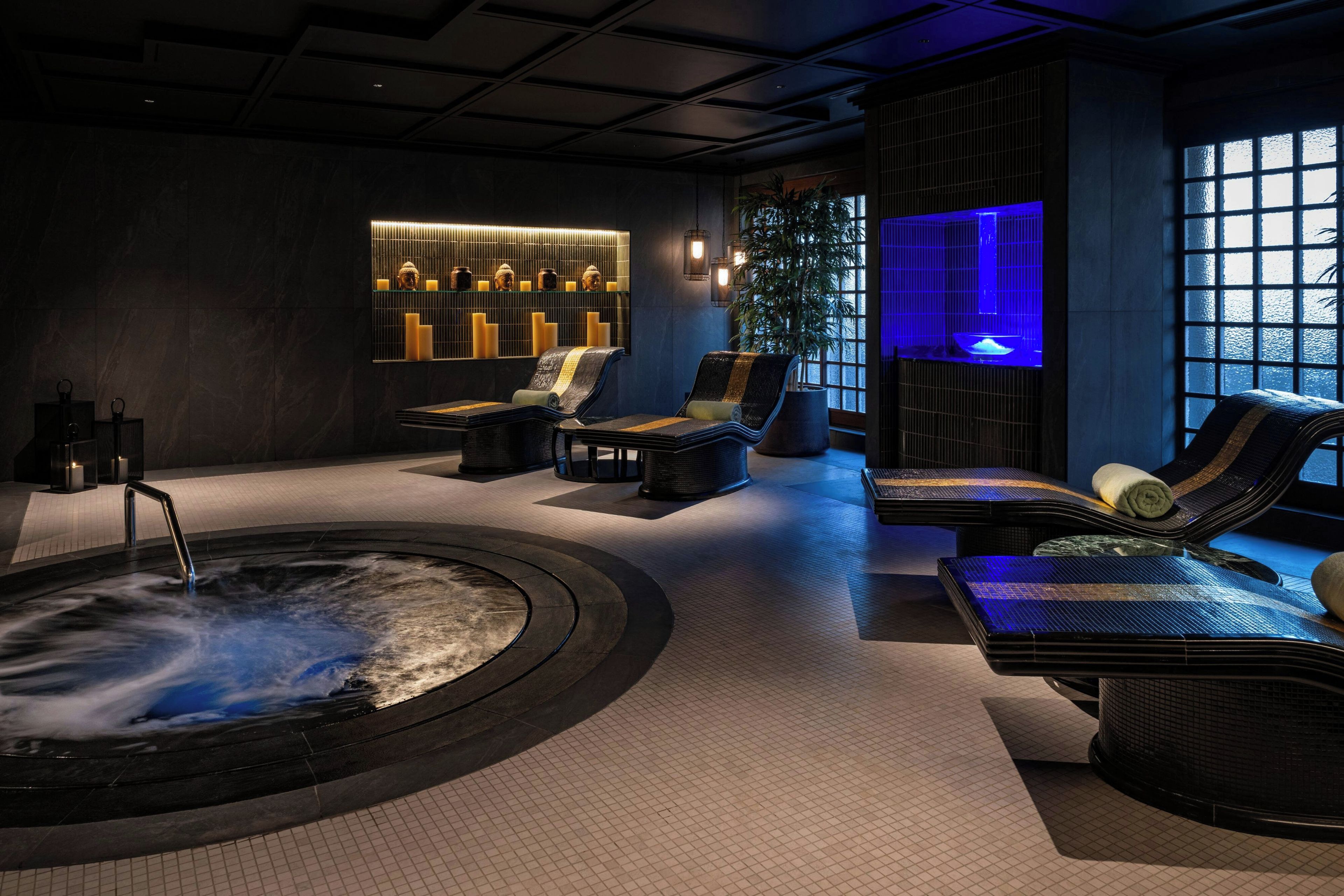 A spa area with a hot tub, lounge chairs, and a wall with candles and Buddha statues.