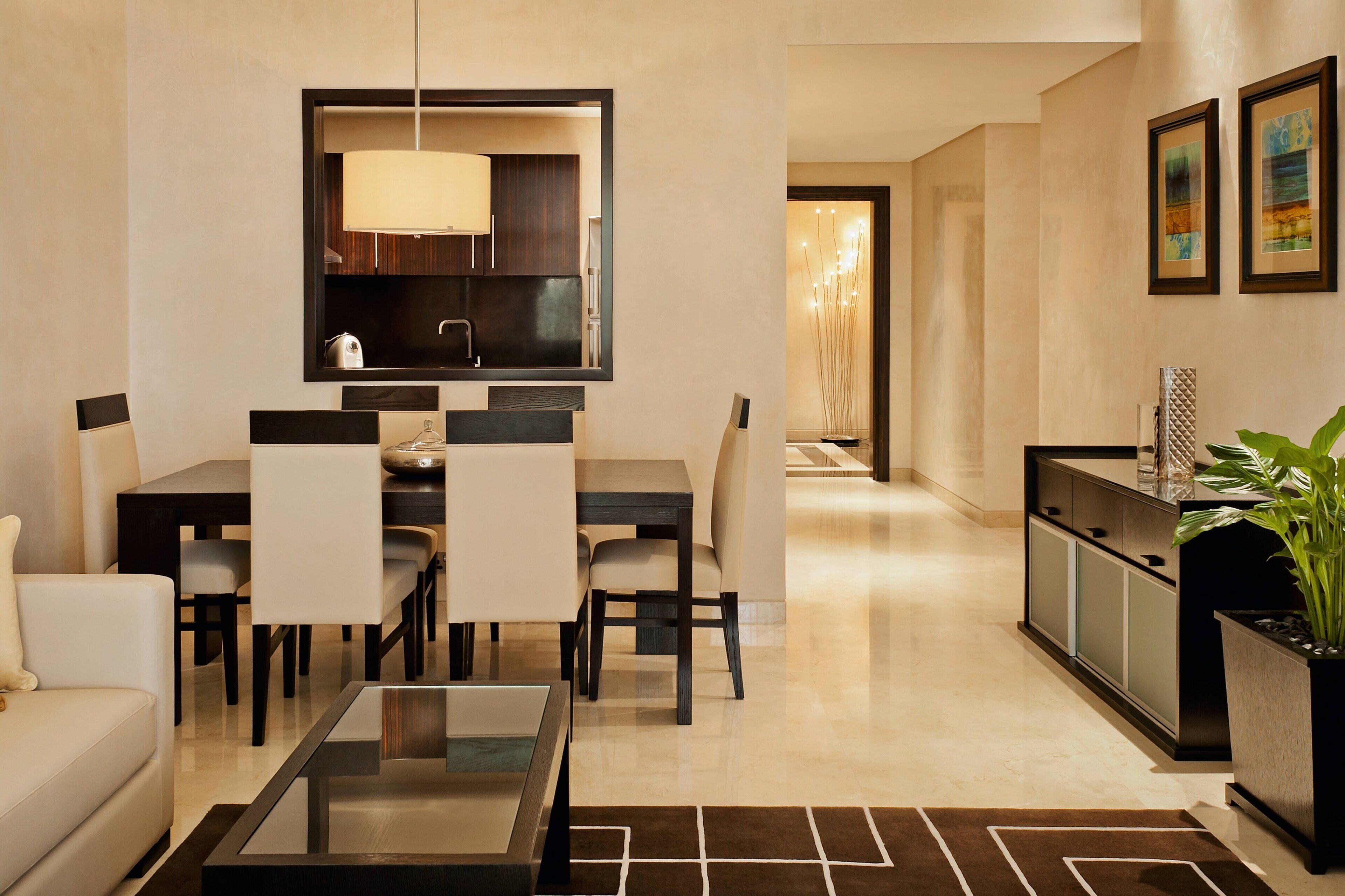 A modern living room with a dining area, a kitchen, and a hallway leading to a bedroom.
