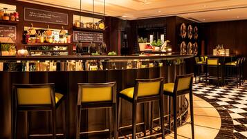 A bar area with a checkered floor, bar stools, and a counter displaying various bottles and jars.