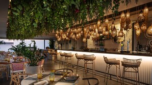 A restaurant with a bar area, wooden chairs, tables, hanging plants, and unique lighting fixtures. - Grosvenor House, a Luxury Collection Hotel, Dubai (Dubai)