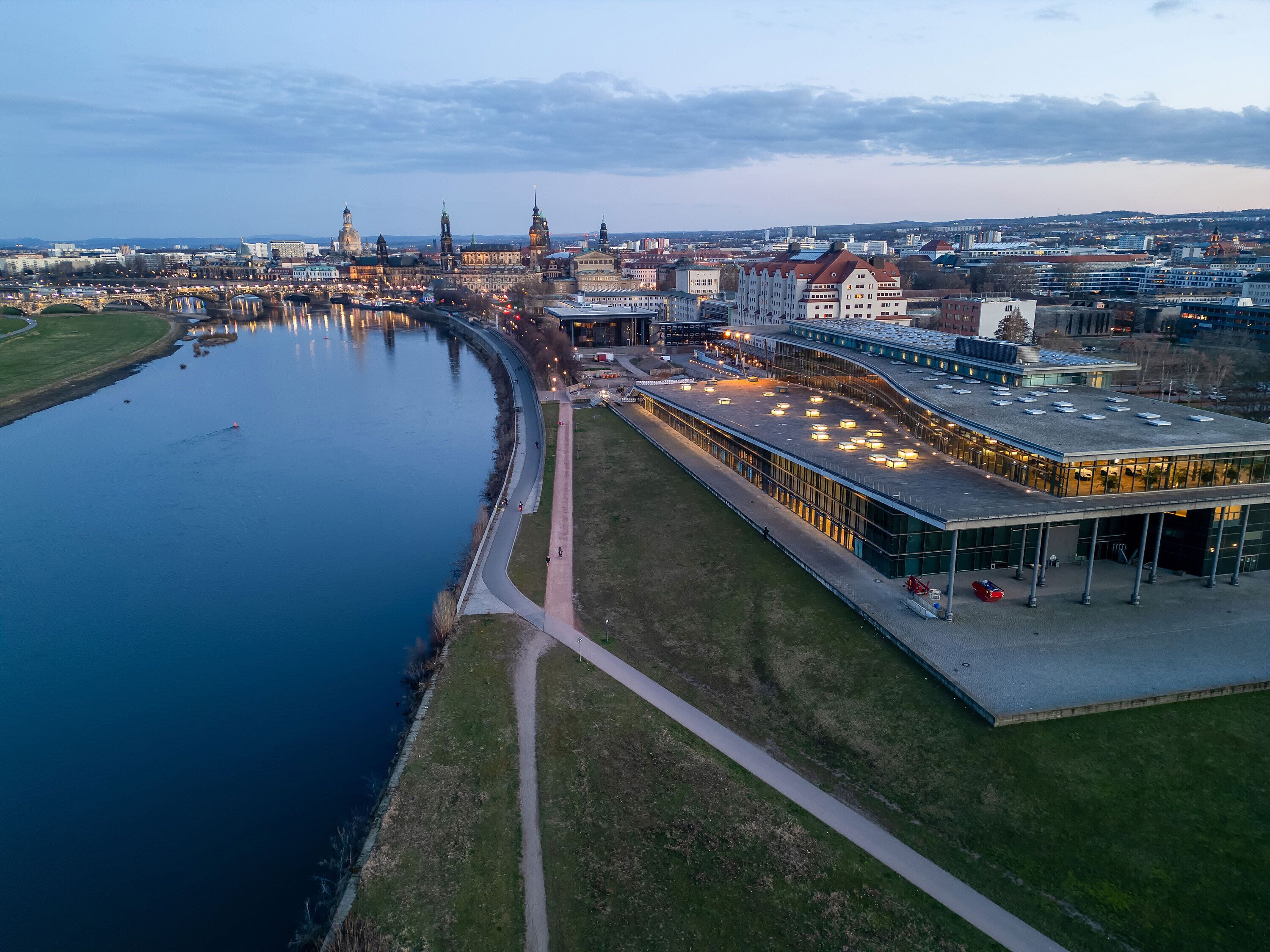 Ein Luftbild einer Flusslandschaft mit einer modernen Gebäude mit Glasfassade und einem Fußgängerweg am Flussufer.