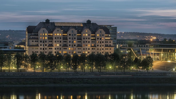 Een groot hotel met meerdere verdiepingen en balkons, gelegen aan een waterpartij met bomen op de voorgrond.