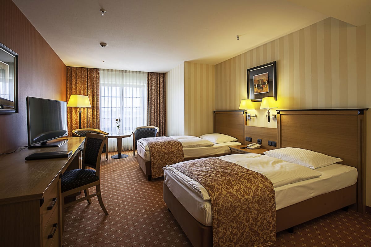 A hotel room with two beds, a desk with a computer, a chair, and a small table.