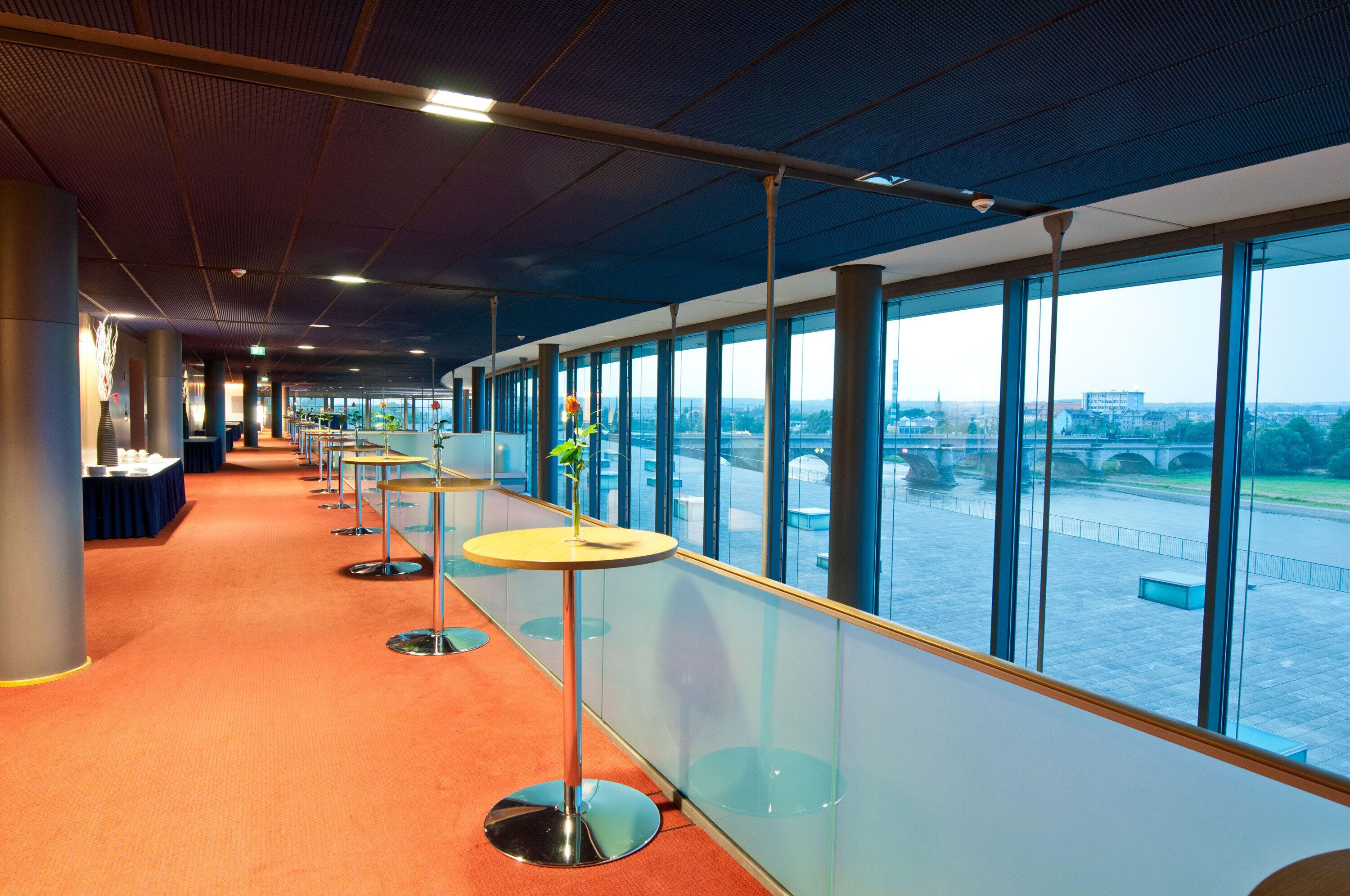 A corridor with tables and chairs, large windows, and a view of a bridge.