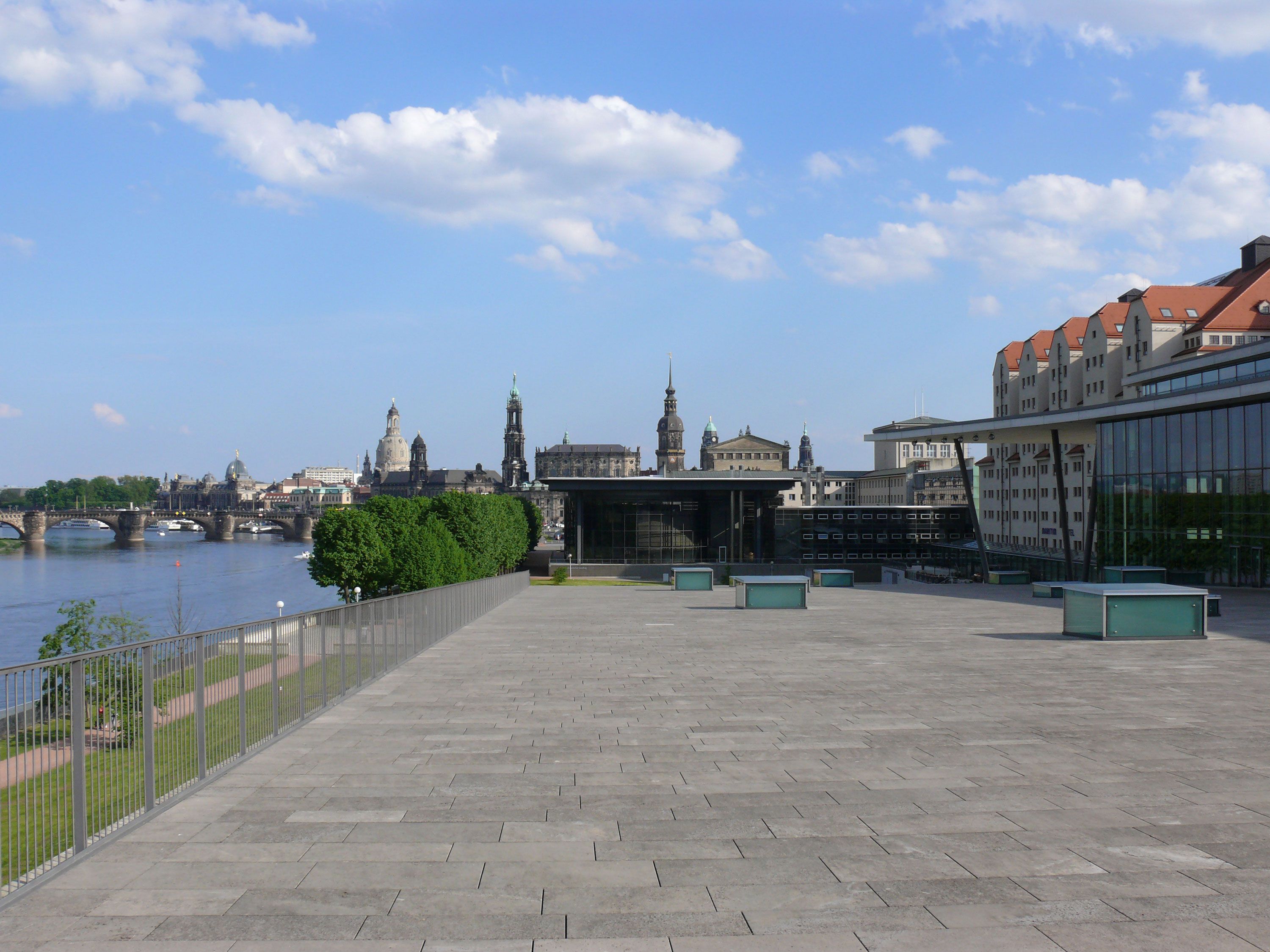 A riverside walkway with a view of historic buildings and a bridge.