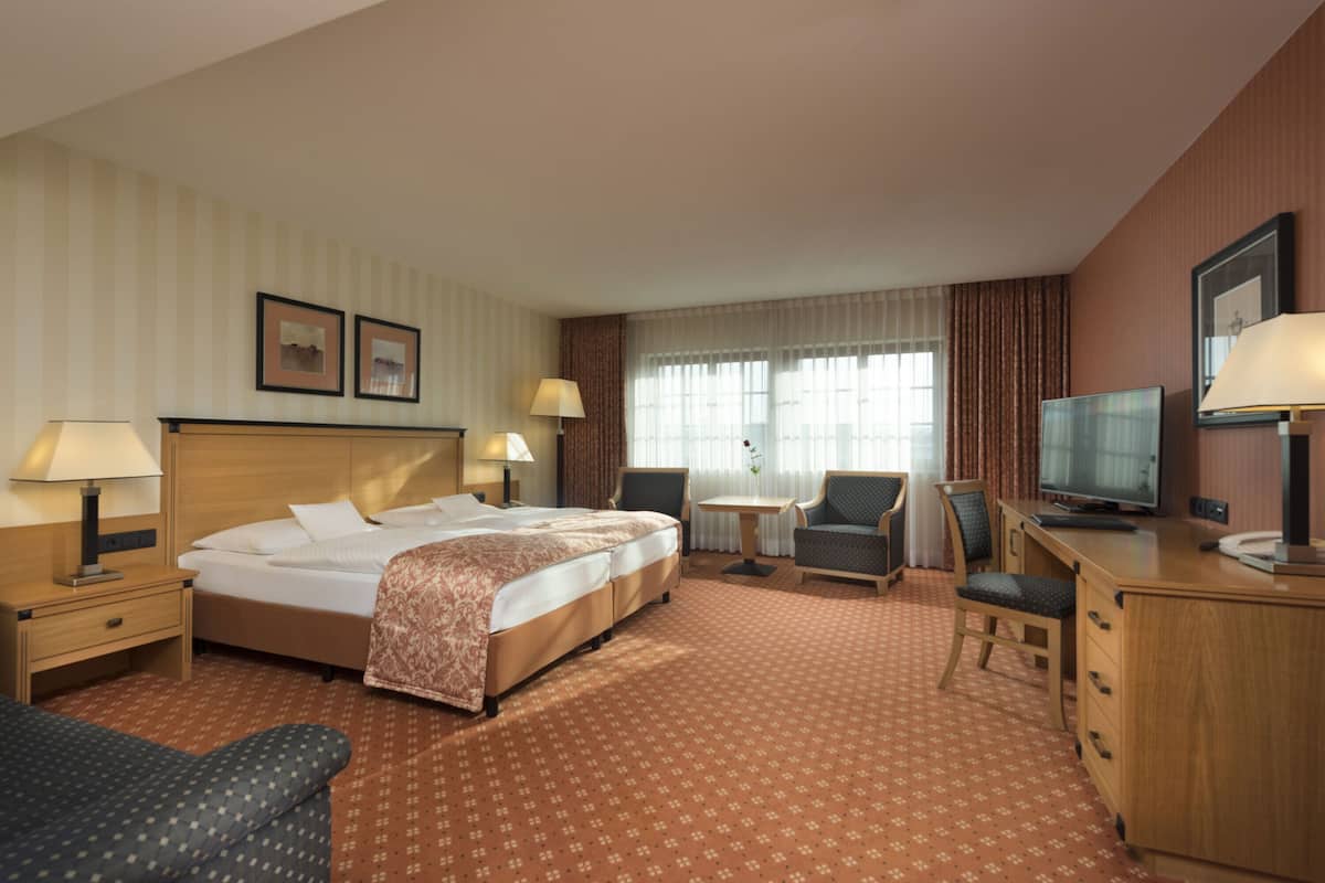 A hotel room with a large bed, two bedside tables with lamps, a desk with a television, a chair, and a small table.