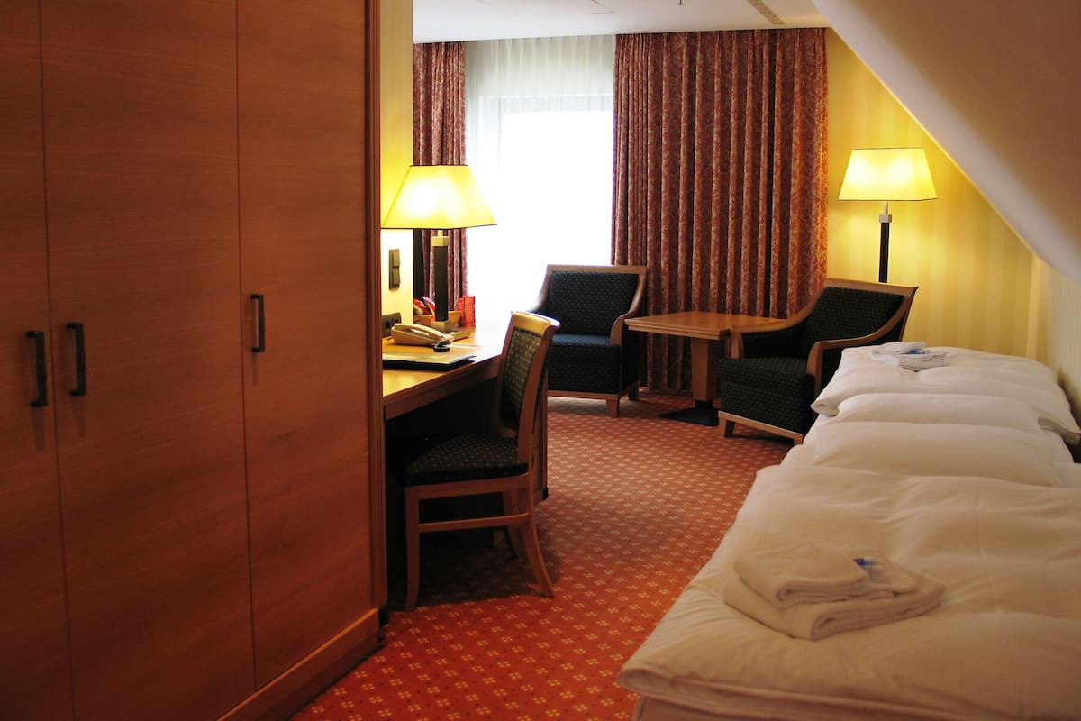 A hotel room with a bed, two chairs, a desk, and a lamp.