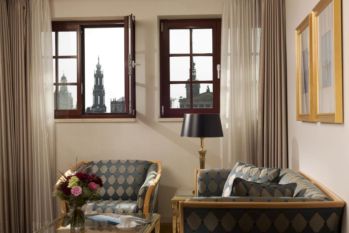 A room with two windows, a sofa, a chair, a lamp, and a vase with flowers.
