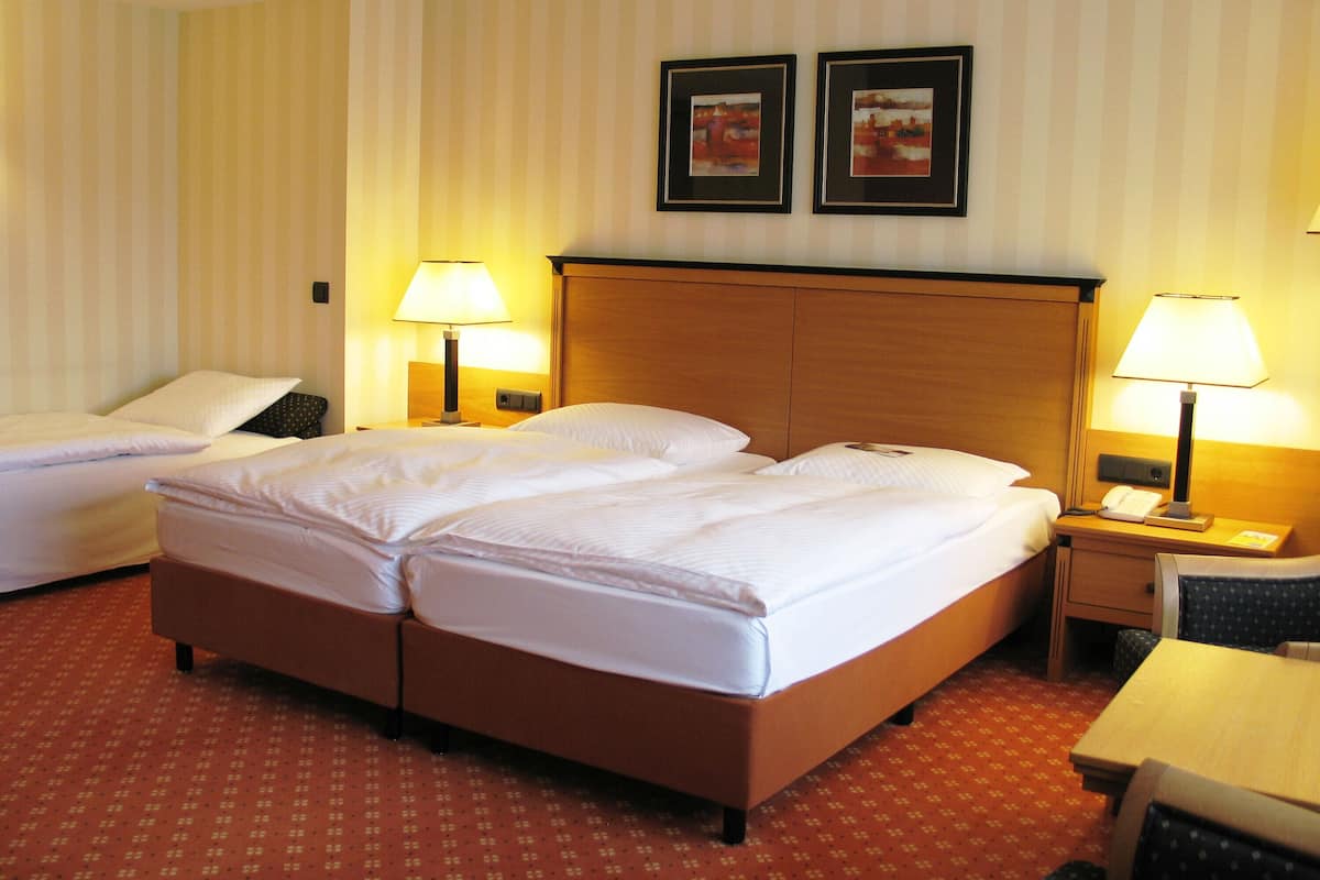 A hotel room with two single beds, a wooden headboard, two bedside lamps, a small table, and two framed pictures on the wall.
