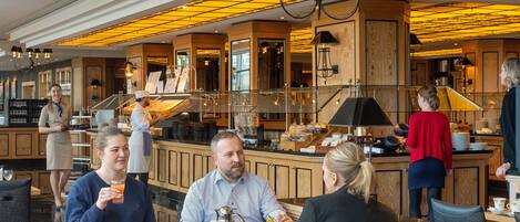 Interior de un restaurante con barra, asientos y mostrador donde un camarero atiende a los clientes.