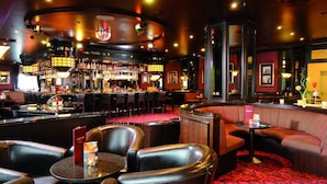 Een bar met lederen zitmogelijkheden, een bargedeelte en een kamerbreed tapijt met dessin.