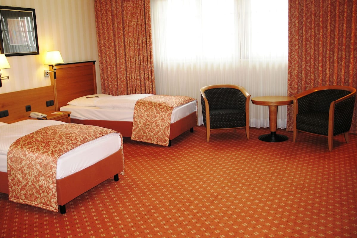 A hotel room with two beds, a chair, a table, and a lamp.