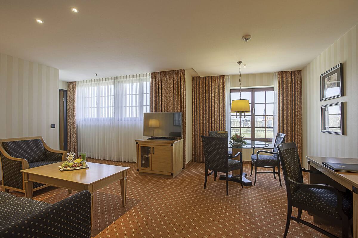 A hotel room with a sofa, a dining table, a TV, and a desk.