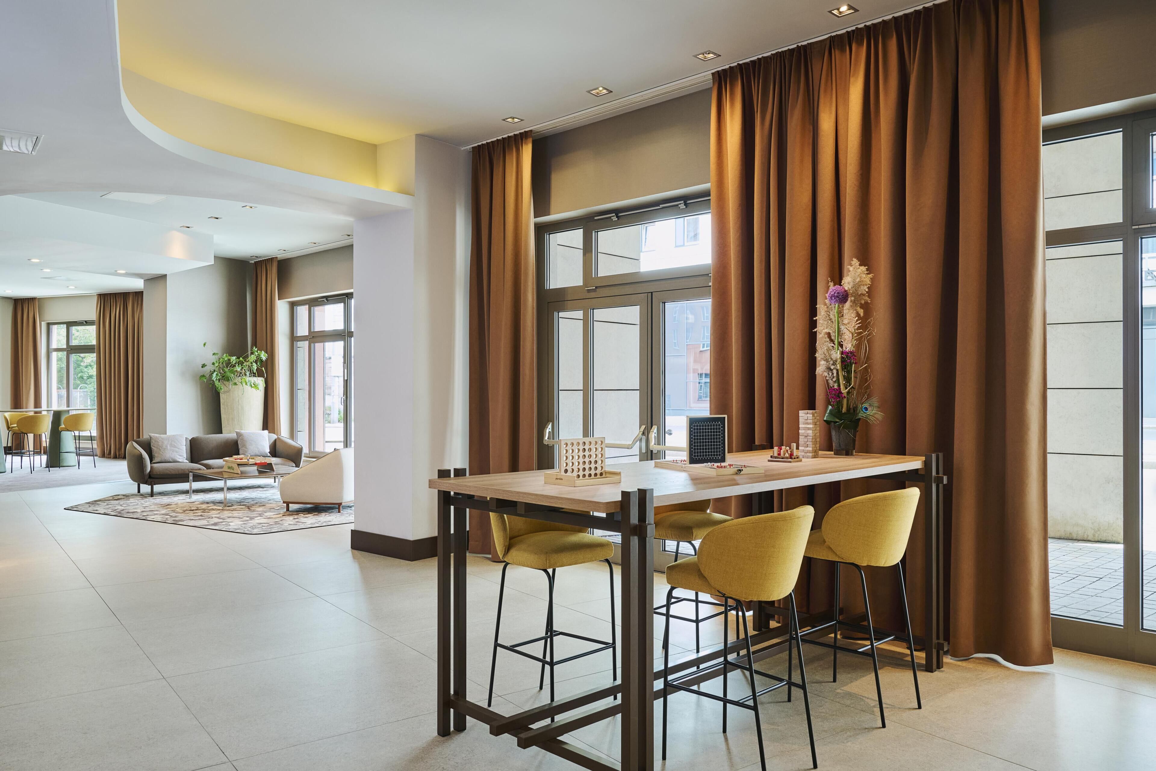 Un moderno vestíbulo de hotel con zona de comedor, ventanas amplias y una planta.