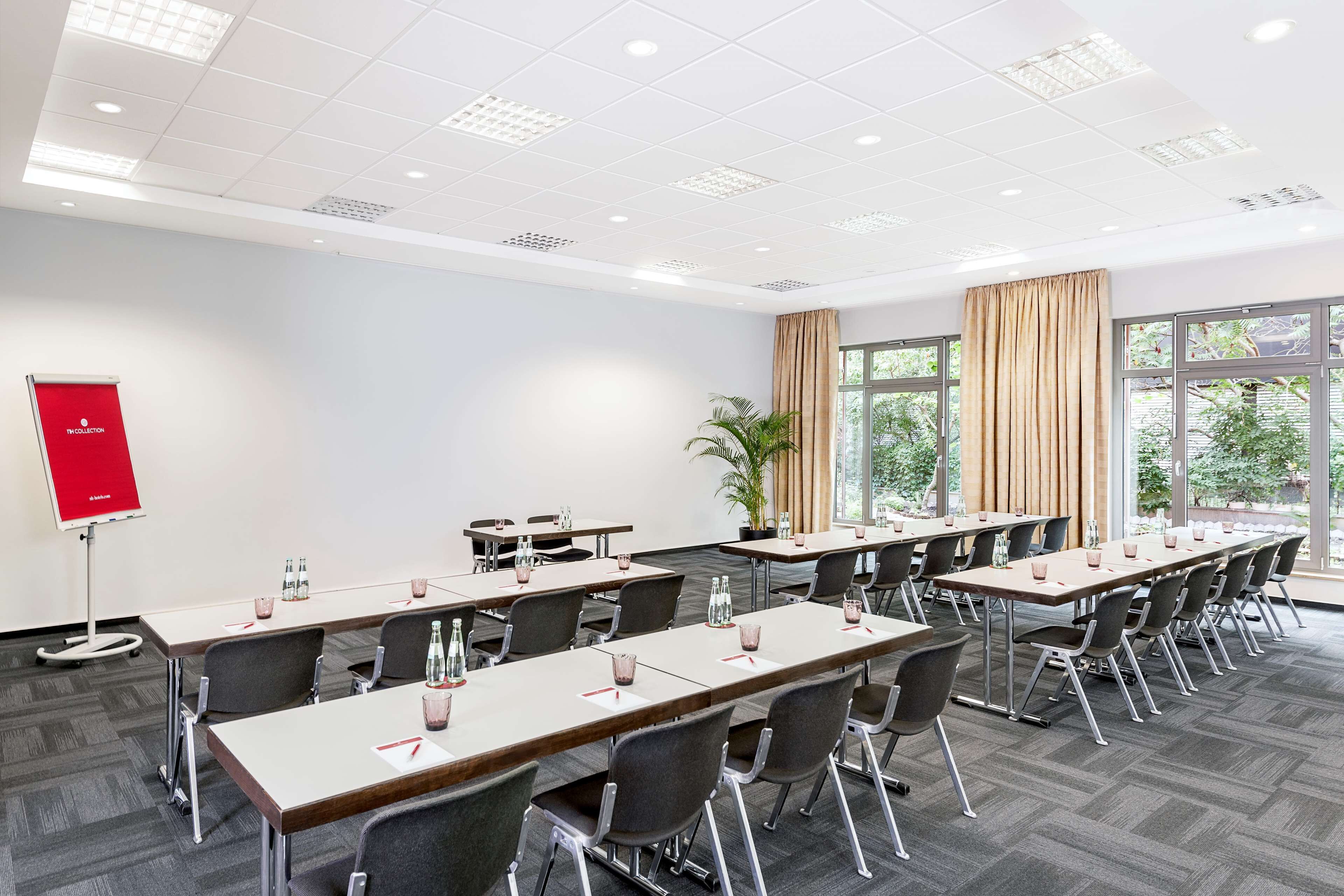 A conference room with multiple tables and chairs, a red flip chart, and large windows with curtains.