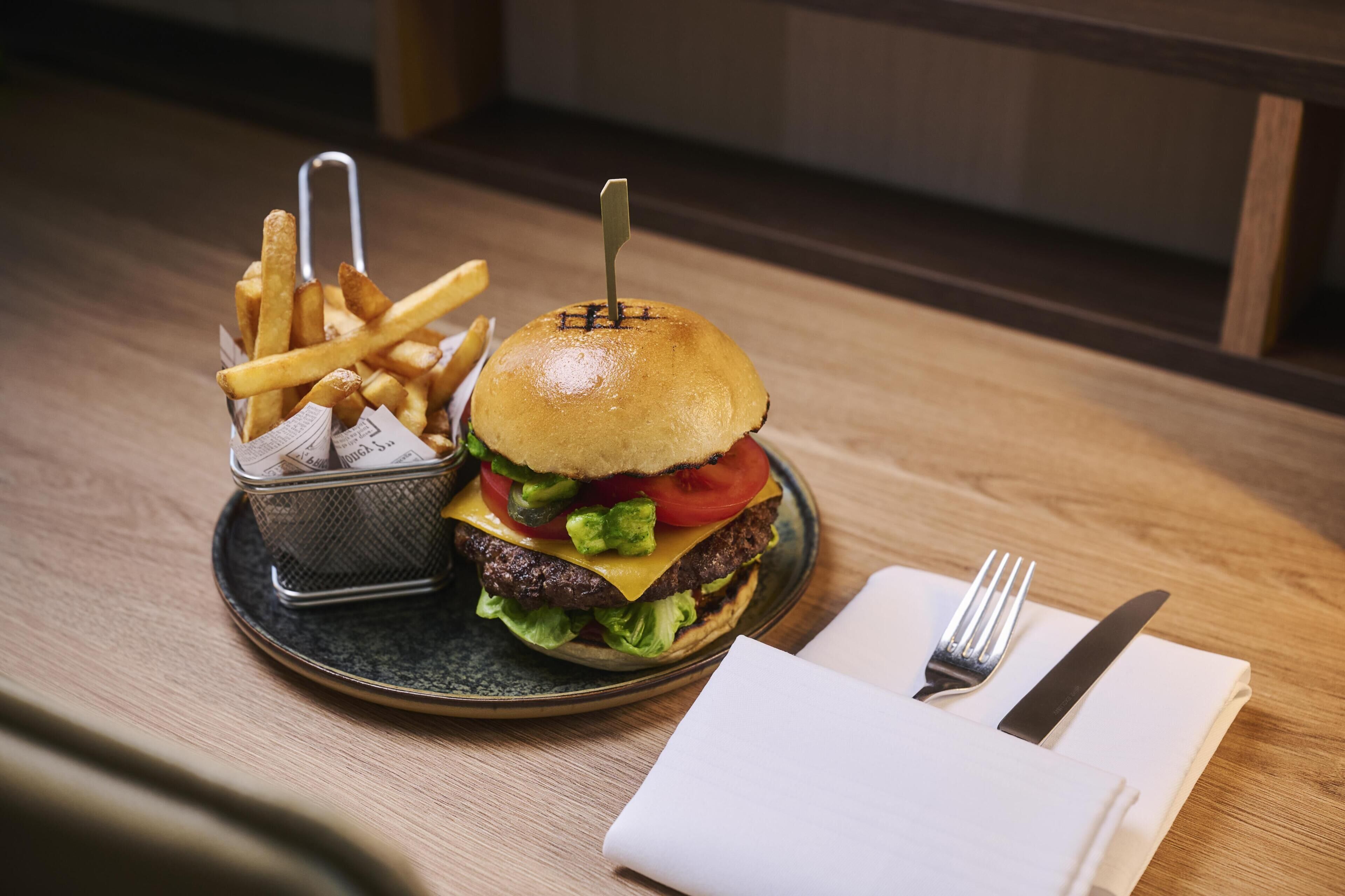 A meal consisting of a burger and fries on a plate, with a fork and knife on a napkin beside it.