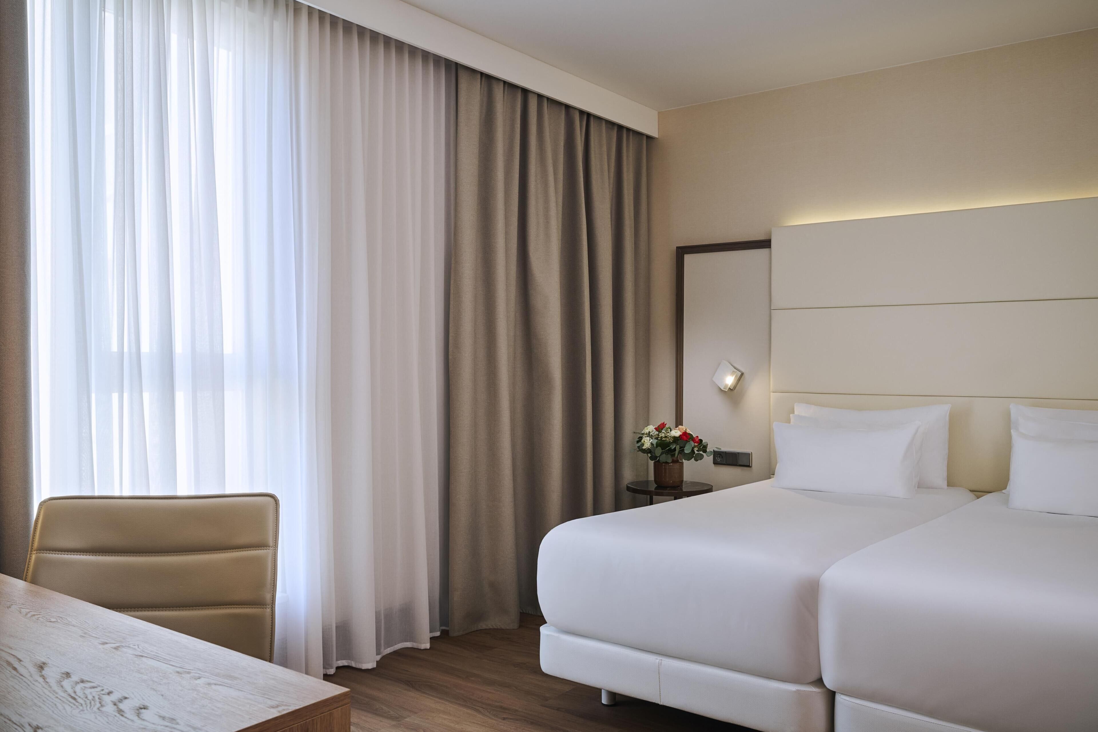 Habitación de hotel con cama, una silla, una mesa y ventana con cortinas.