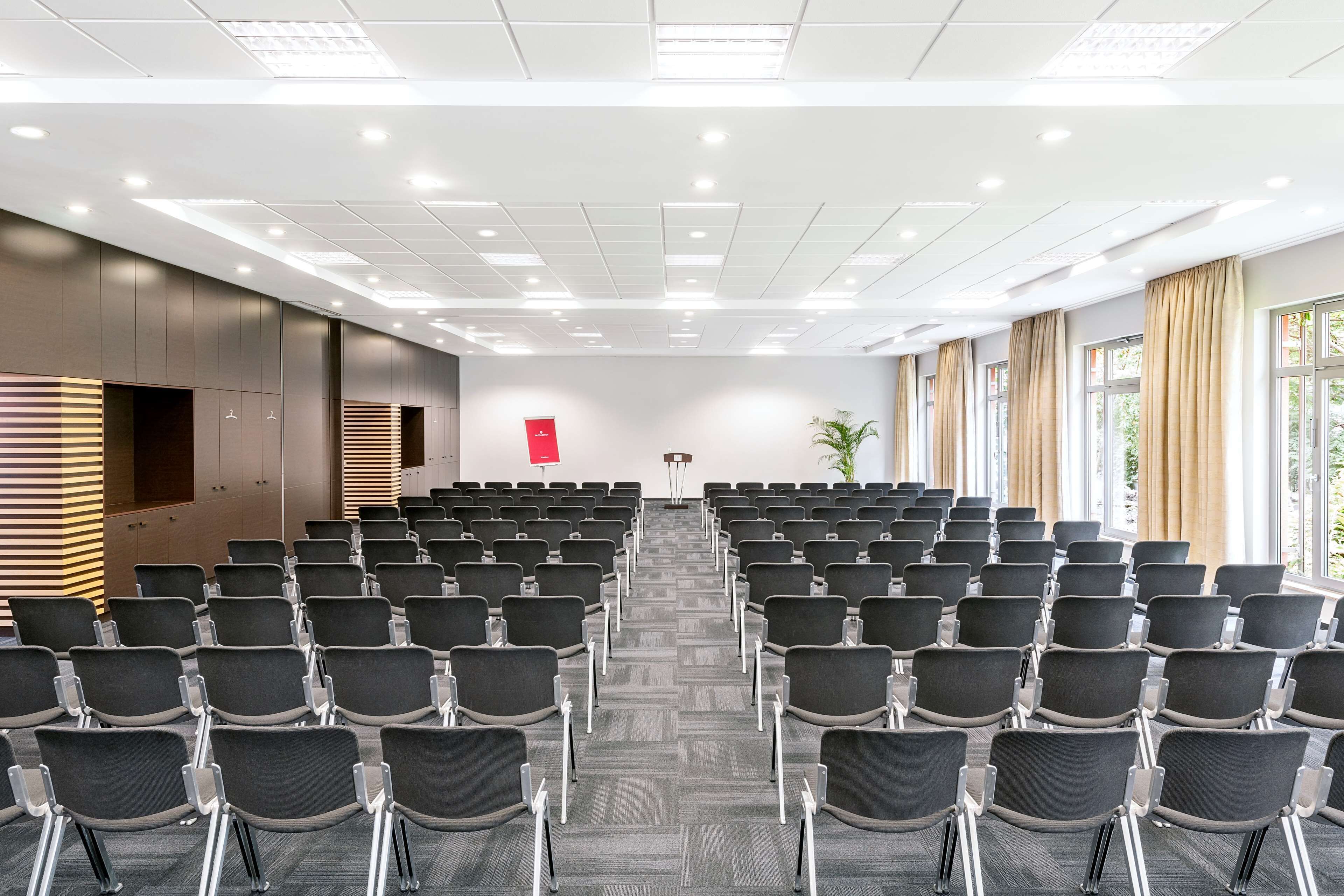 A conference room with rows of chairs, a podium, and a large window with curtains.