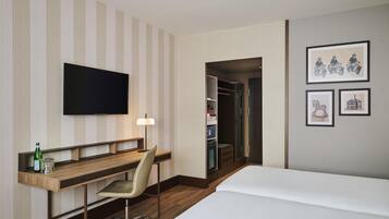A hotel room with a bed, a desk with a chair, a television, and framed pictures on the wall.