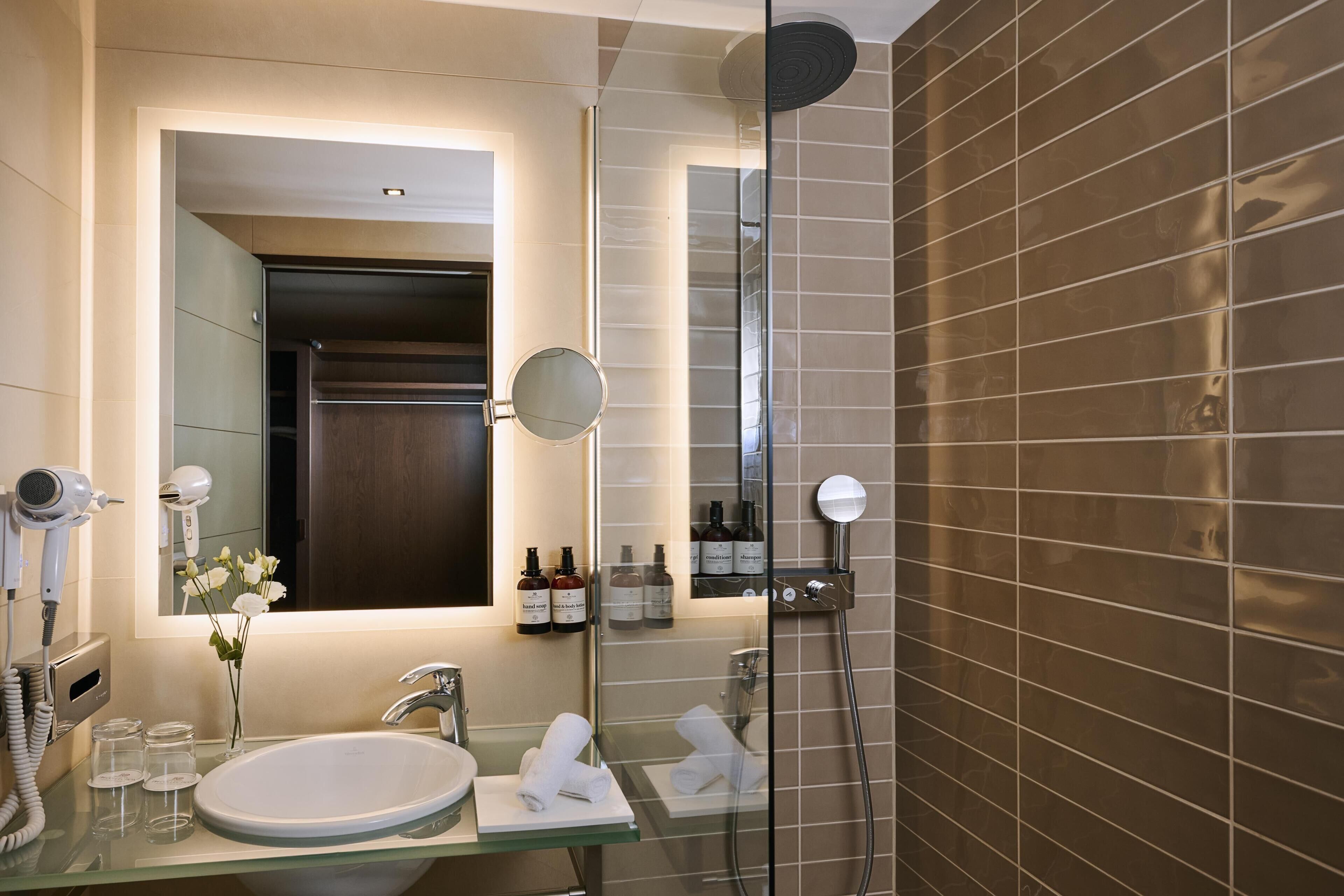 A modern bathroom with a glass-enclosed shower, a sink with a mirror, and a hairdryer on the wall.
