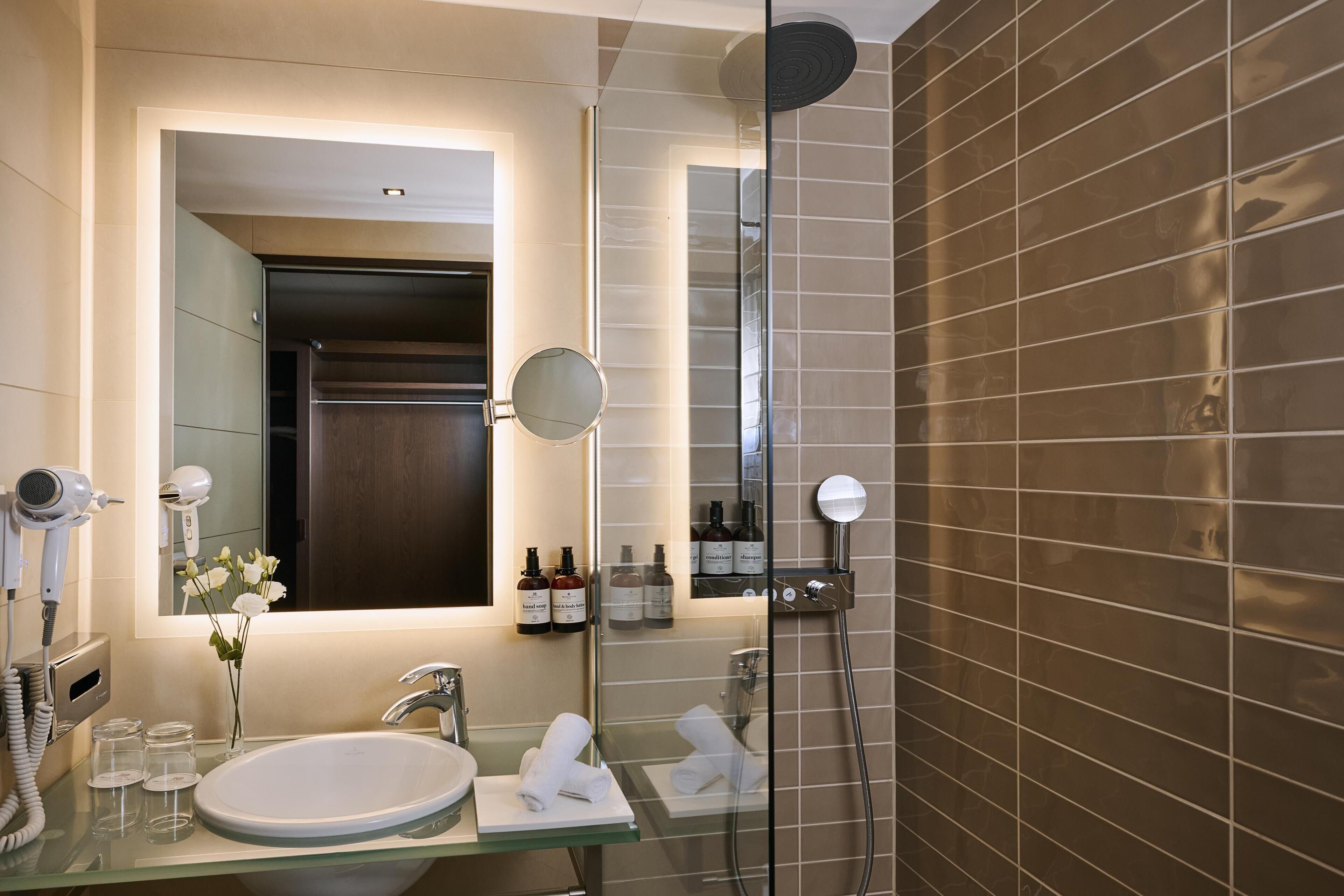 Un baño moderno con cabina de ducha de vidrio, un lavamanos con espejo y artículos de tocador en la encimera.