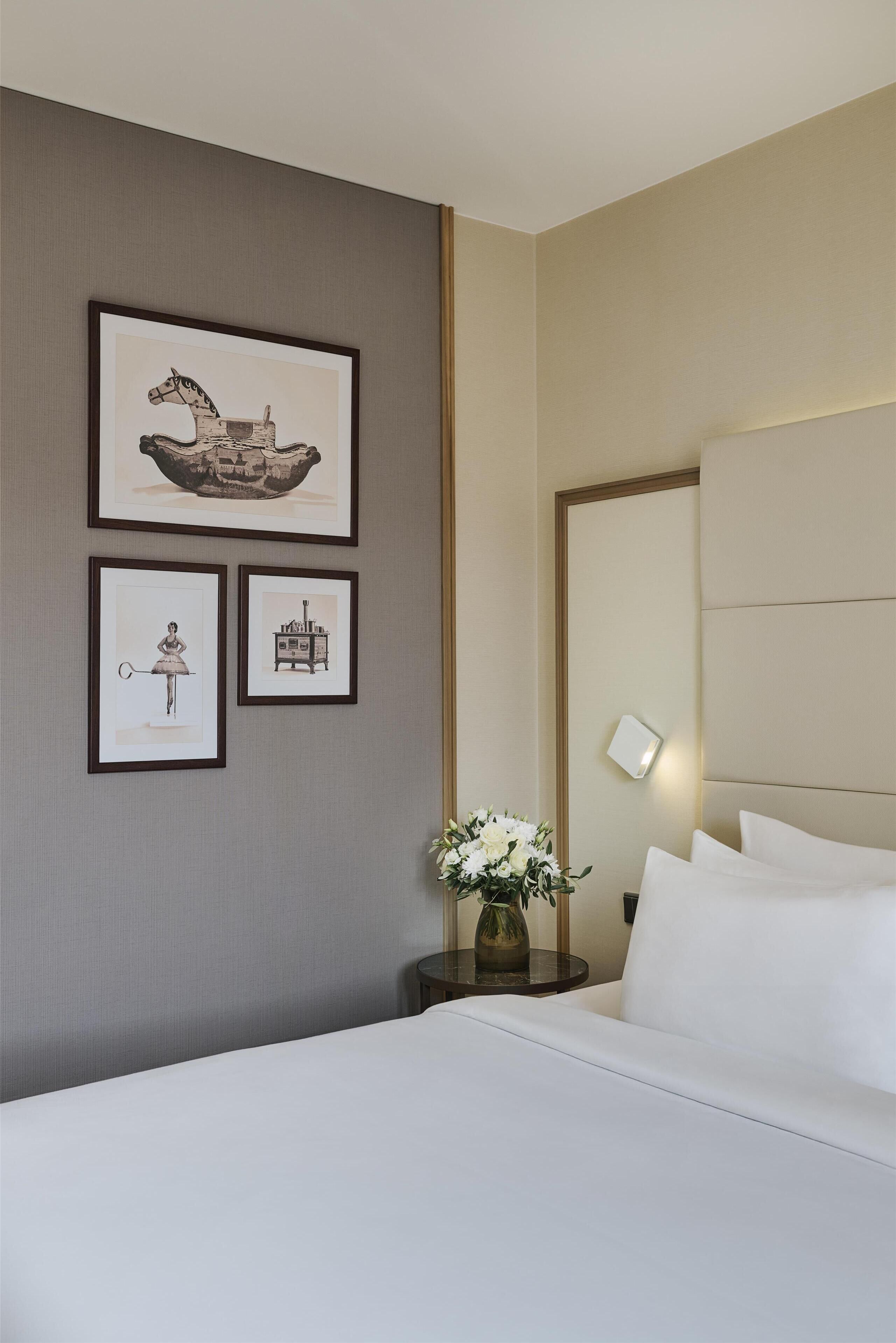 A hotel room with a large bed, a nightstand with a vase of flowers, and three framed pictures on the wall.