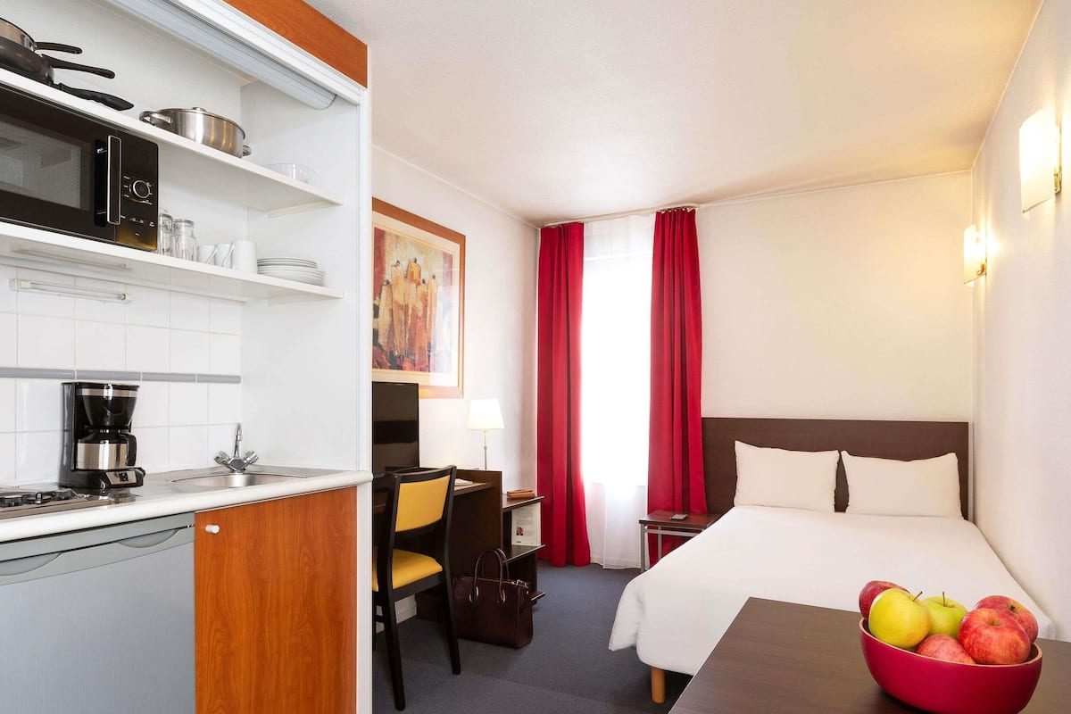 A hotel room with a bed, a desk with a bowl of fruit, a chair, a desk lamp, a coffee maker, a microwave, and a TV.