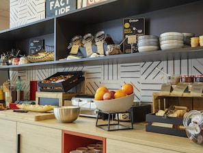 A breakfast bar with jars of spreads, a bowl of fruit, and a coffee machine.
