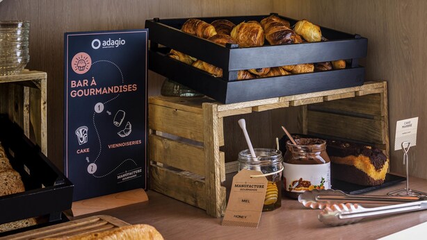 A bakery display with pastries, a sign for 'Bar à Gourmandises,' and a jar of honey.