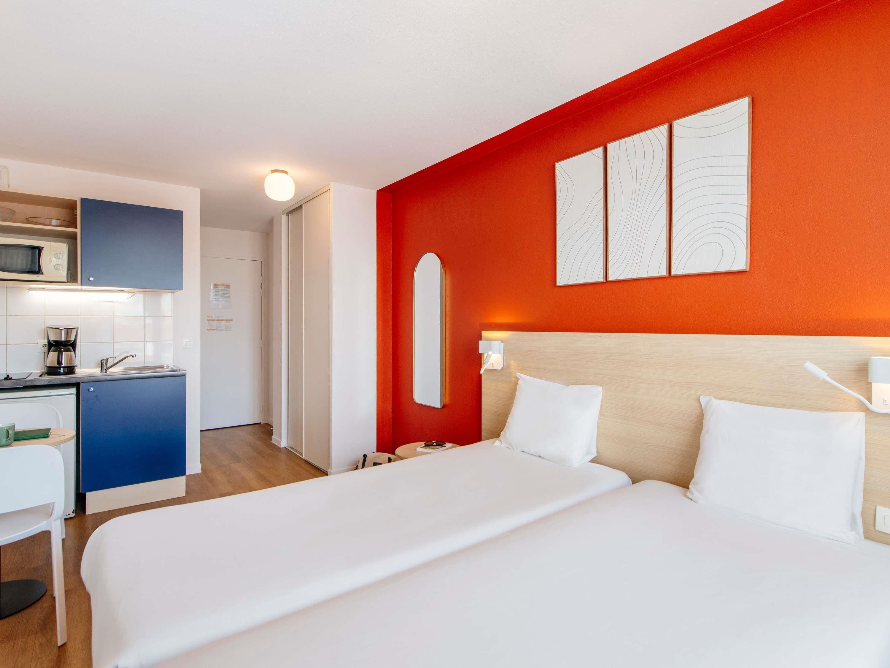 A hotel room with a bed, bedside table, and a kitchenette area.