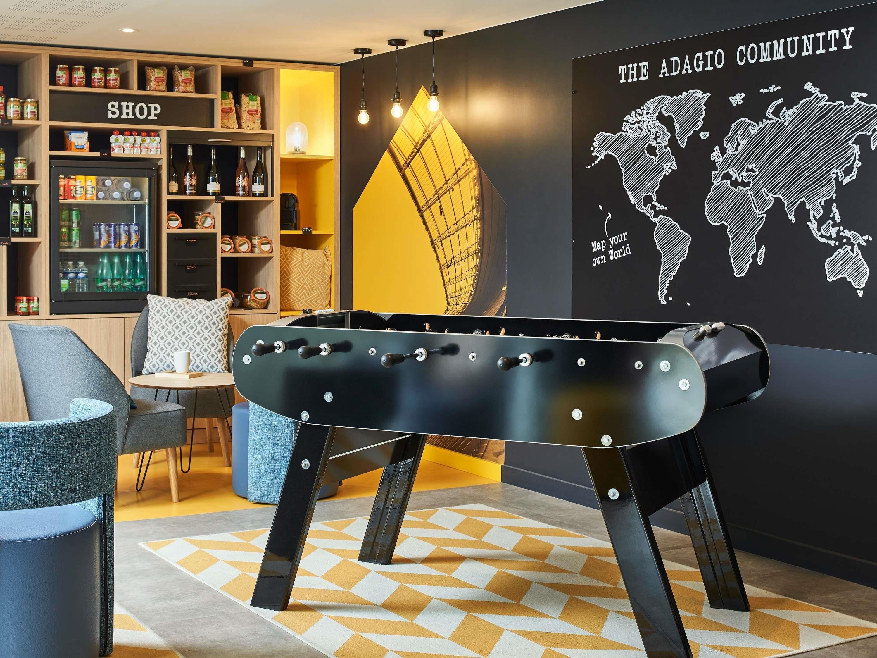 A pool table in a room with a 'SHOP' sign, a world map mural, and a cozy seating area.
